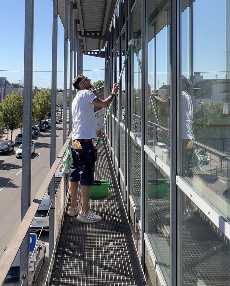 Fensterreinigung an der Glasfassade eines Bürogebäudes von einem Laufsteg in der zweiten Etage aus.