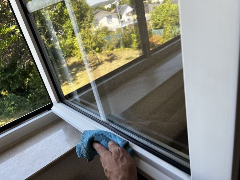 Nahaufnahme: Reinigung von Rahmen und Falz eines Fensters mit einem Mikrofasertuch.